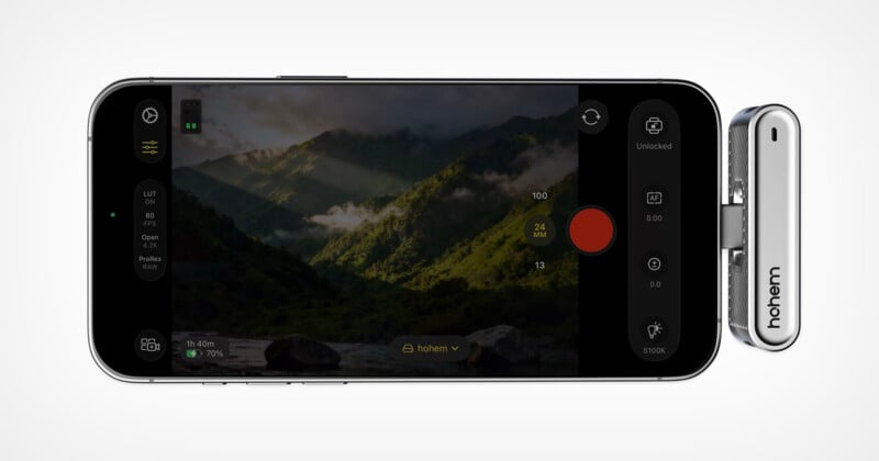 Smartphone que muestra la interfaz de la aplicación de la cámara en modo horizontal capturando hermosas vistas de montañas verdes con luz solar y nubes. Los dispositivos plateados están marcados "alto" Pégalo en el costado del teléfono.