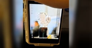 A close-up of a digital camera screen shows a blurred photo being reviewed, with camera settings and icons visible on the display and a hand partly visible at the top.