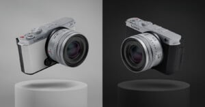 Two compact Panasonic Lumix cameras are displayed, one in white on a light gray background and one in black on a dark gray background, both hovering above cylindrical pedestals.