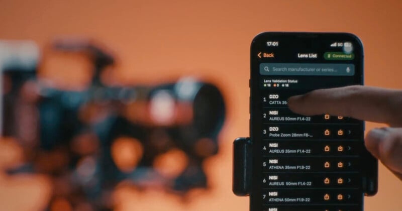 Una mano sostiene un teléfono inteligente que muestra una lista de tomas en la aplicación con configuraciones de cámara profesional borrosas en segundo plano sobre un fondo naranja.
