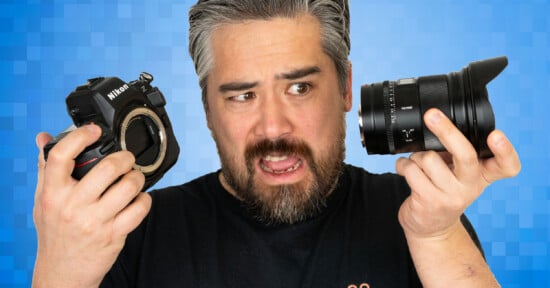 A man with gray hair and beard looks confused while holding a Nikon camera body in one hand and a camera lens in the other against a blue pixelated background.