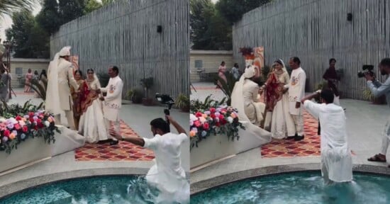 A wedding photoshoot by a pool. A photographer accidentally falls into the water as the bride and groom, dressed in traditional attire, pose with two men on a colorful rug near a flower arrangement.