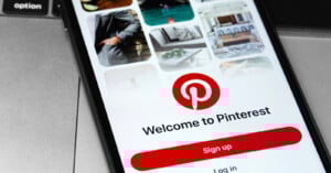 A smartphone screen displays the Pinterest app welcome page with the red Pinterest logo, "Welcome to Pinterest" text, and a prominent "Sign up" button. Blurred images of pins appear at the top of the screen.