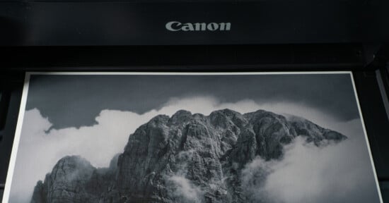 A black-and-white photograph of a mountain surrounded by clouds is being printed from a Canon printer.