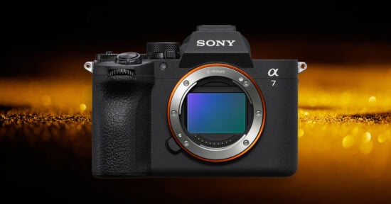 A Sony Alpha 7 mirrorless camera body is shown facing forward against a dark background with a golden light effect behind it.
