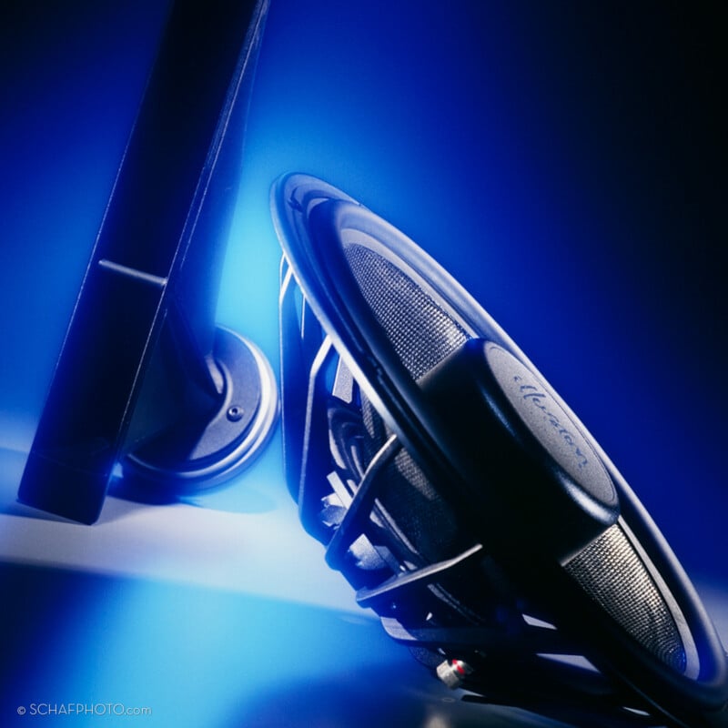 A close-up of a black audio speaker and its mounting arm, dramatically lit with blue highlights and shadows, creating a modern and high-tech atmosphere.
