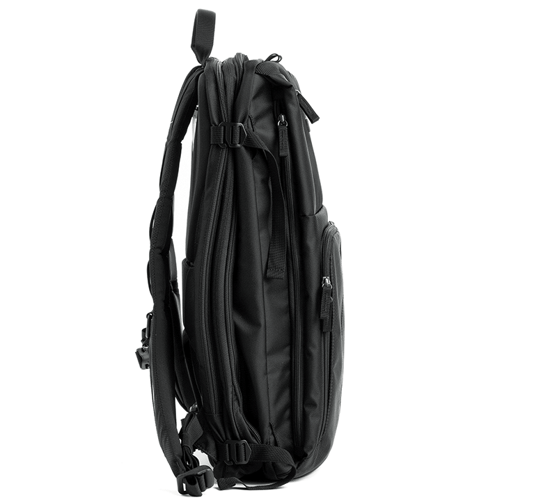 Vista lateral de una mochila negra con múltiples compartimentos con cremallera, correas acolchadas ajustables y hebillas. El bolso se alza sobre un fondo blanco puro.