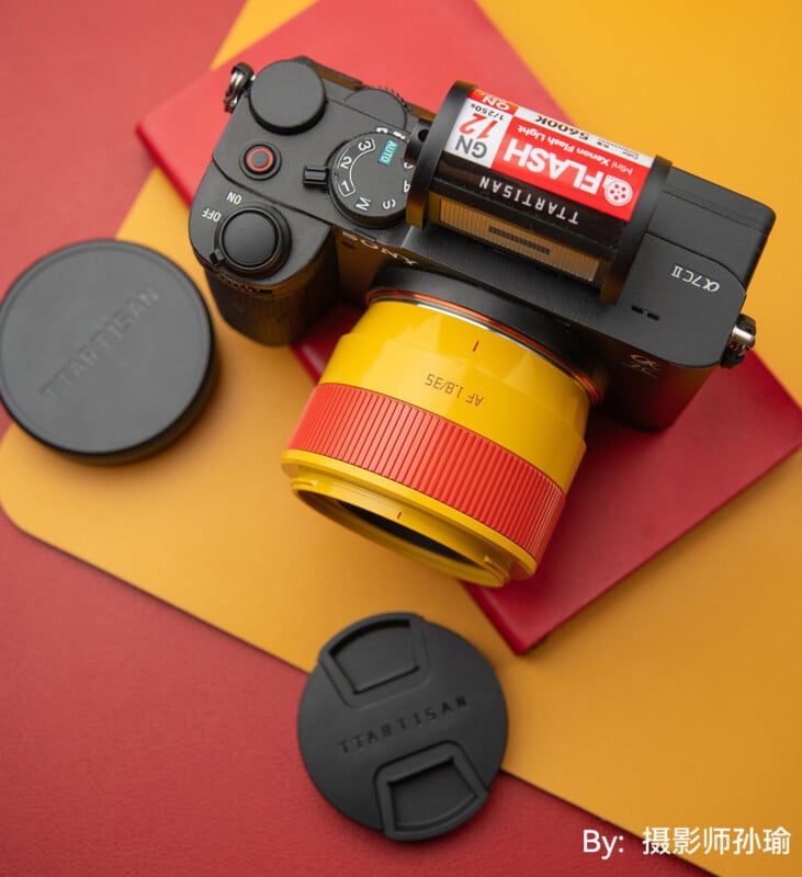 Una cámara sin espejo con una lente amarilla y roja y un rollo de película Kodak TMAX encima colocada sobre una superficie roja y amarilla. Las dos tapas de lentes negras están marcadas "En TTArtisan" Todo cerca. El texto chino está en la esquina inferior derecha.