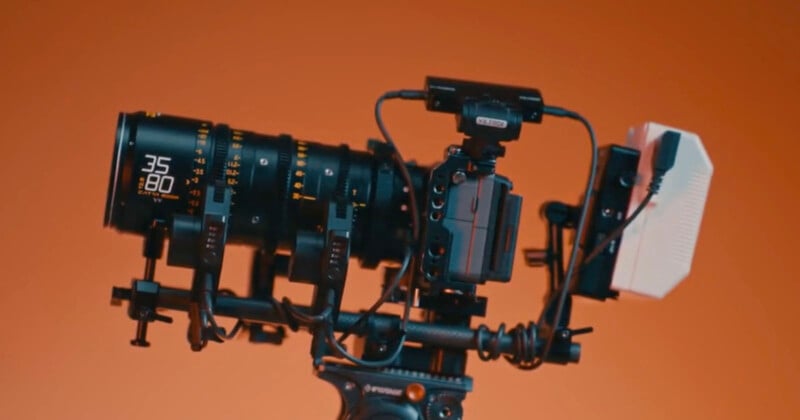 Equipo de cámara de cine profesional con lente de 35 mm, varios cables de conexión, monitores y accesorios, aislados sobre fondo naranja.