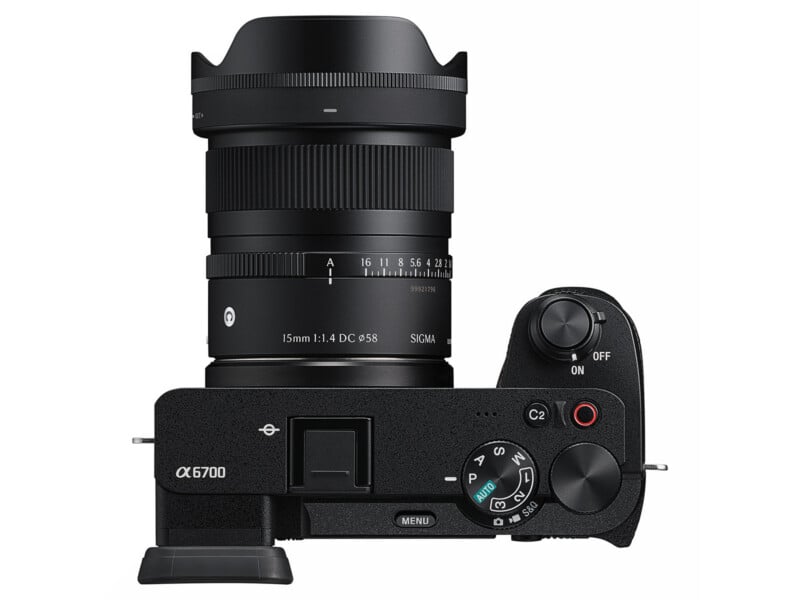 Top view of a black Sony Alpha 6700 mirrorless camera with a Sigma 15mm f/1.4 DC DN lens attached. The camera’s control dials, buttons, and on/off switch are clearly visible.