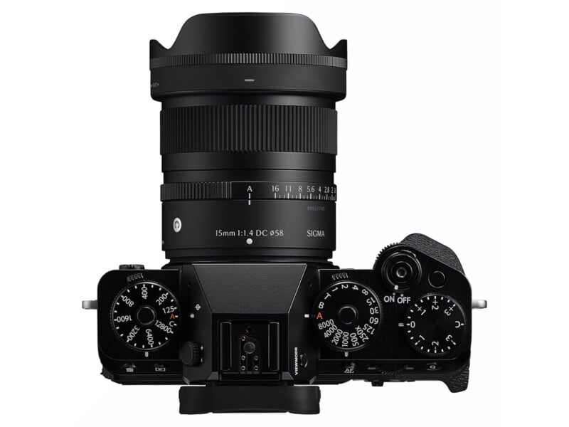 Top view of a black digital camera with dials, buttons, and a Sigma 16mm f/1.4 DC DN lens attached. The camera is turned slightly to the right and the lens hood is mounted.