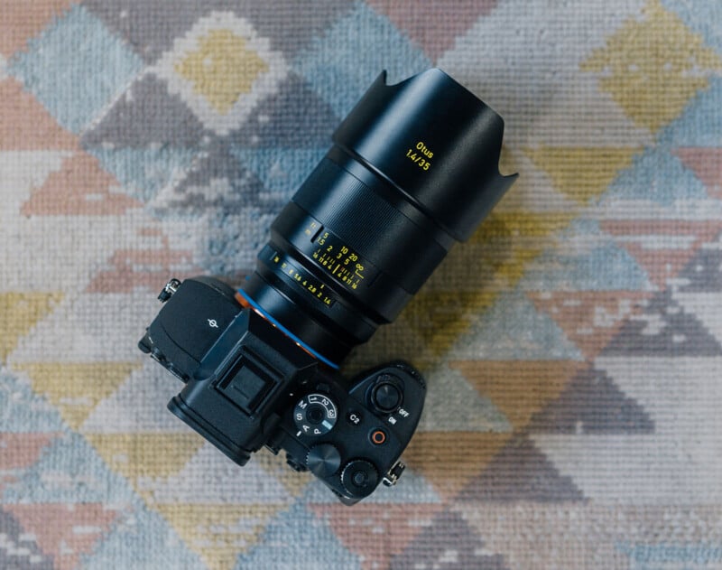 A black digital camera with a large lens labeled "Distagon 1.4/35" sits on a patterned, multicolored rug with geometric designs. The camera is viewed from above.