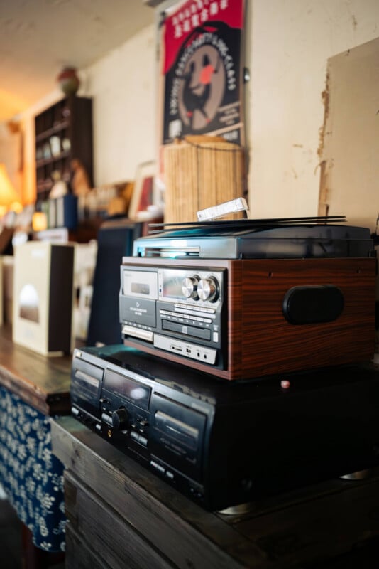 A vintage wooden turntable and stereo system sit on a table in a cozy room, surrounded by books, records, and warm decor.