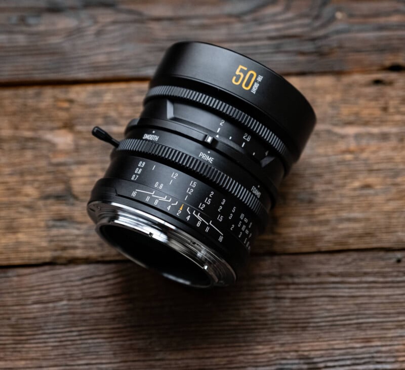 A black 50mm camera lens with white and yellow markings lies on a rustic wooden surface, showing detailed focus and aperture rings.
