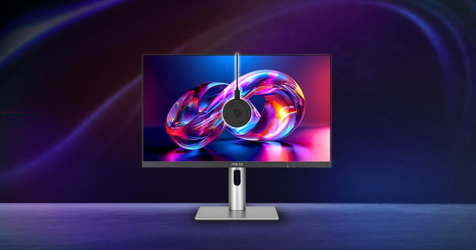 A sleek ASUS monitor displays vibrant abstract digital art, with a round webcam mounted at the center top. The monitor stands on a modern silver base against a dark, colorful, gradient background.
