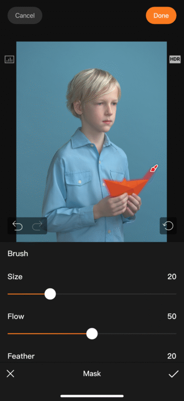 A young boy in a light blue shirt holds an orange paper plane against a blue background. Photo editing tools, including brush size, flow, and feather sliders, are displayed at the bottom of the screen.