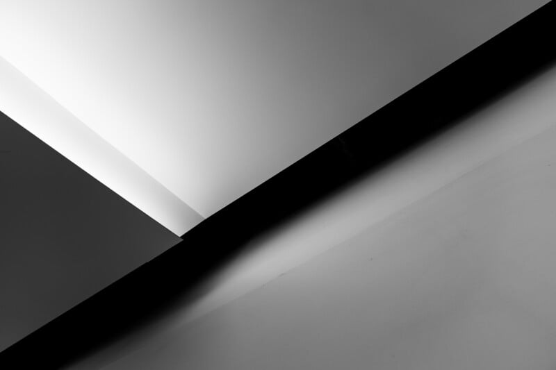 Black and white abstract photo showing sharp geometric lines and angles, with contrasting light and shadow on intersecting walls and ceilings.