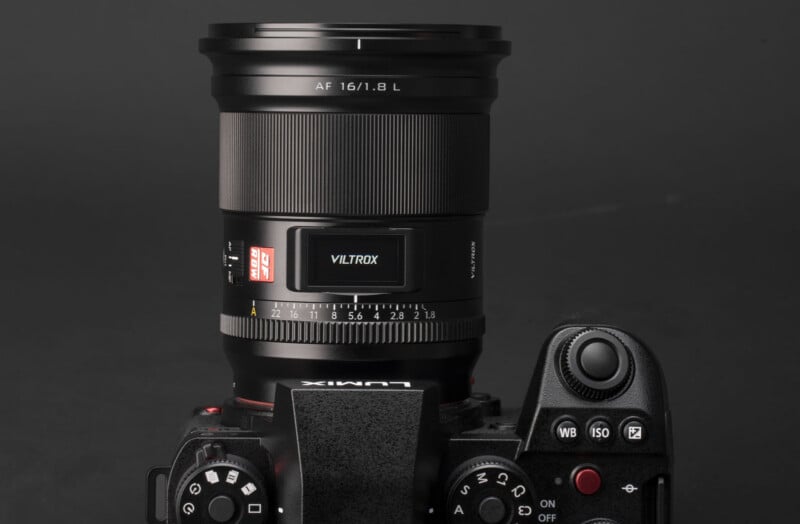 A close-up view of a Lumix camera with a large Viltrox 16mm f/1.8 lens attached, set against a plain dark background. The camera's control buttons and dials are visible.
