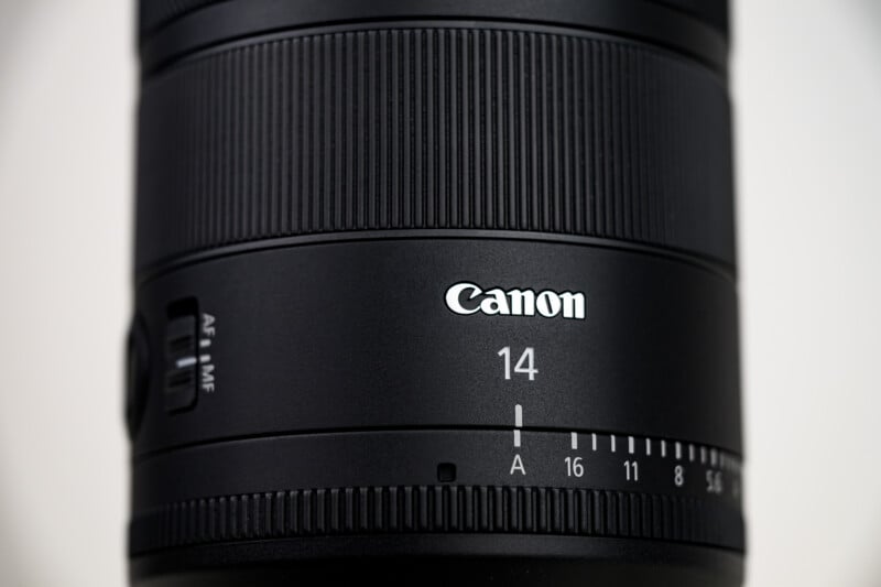 Close-up of a black Canon camera lens, showing the Canon logo, the number 14 indicating the focal length, and a switch labeled AF/MF with aperture settings ranging from A to 22.