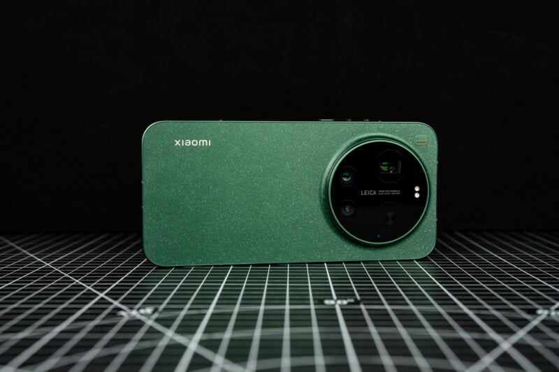 A green Xiaomi smartphone with a large Leica-branded camera module is placed on a black grid-patterned surface, with a dark background.