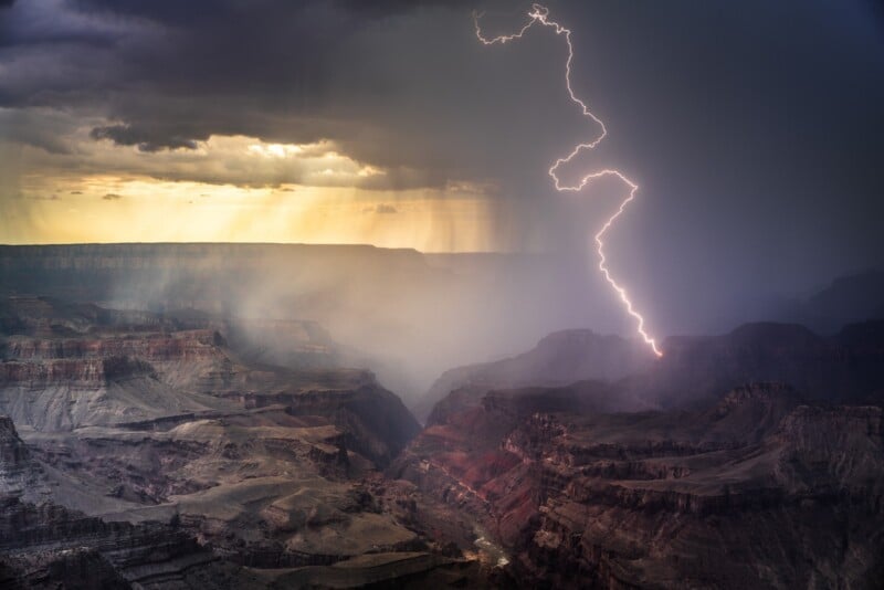 A dramatic lightning bolt strikes the Grand Canyon during a storm, with dark clouds and rain on the right and a golden sunset illuminating canyon cliffs on the left.
