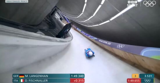 A luge athlete speeds down an icy track at the Winter Olympics. Timings for M. Langenhan (GER) and D. Fischnaller (ITA) are shown on screen, with BBC Sport and Olympic rings logos in the top right corner.