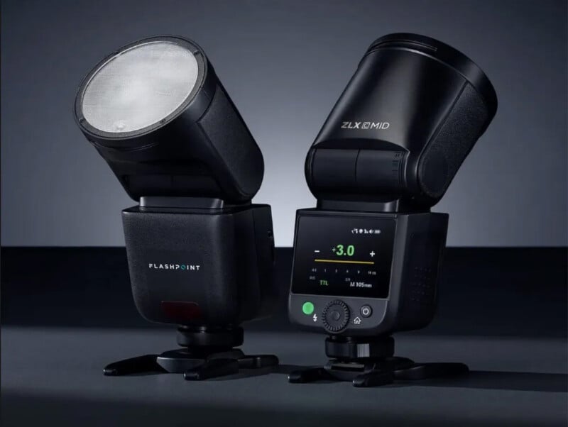 Two black camera flash units, one facing forward showing the bulb and labeled "Flashpoint," the other turned to display an LCD screen with settings and buttons, both set against a dark background.