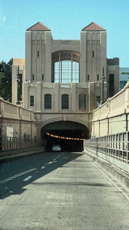 Un automóvil se detiene en un túnel debajo de un gran edificio Art Déco con torres con techo de tejas rojas y ventanas altas que reflejan el cielo azul claro.