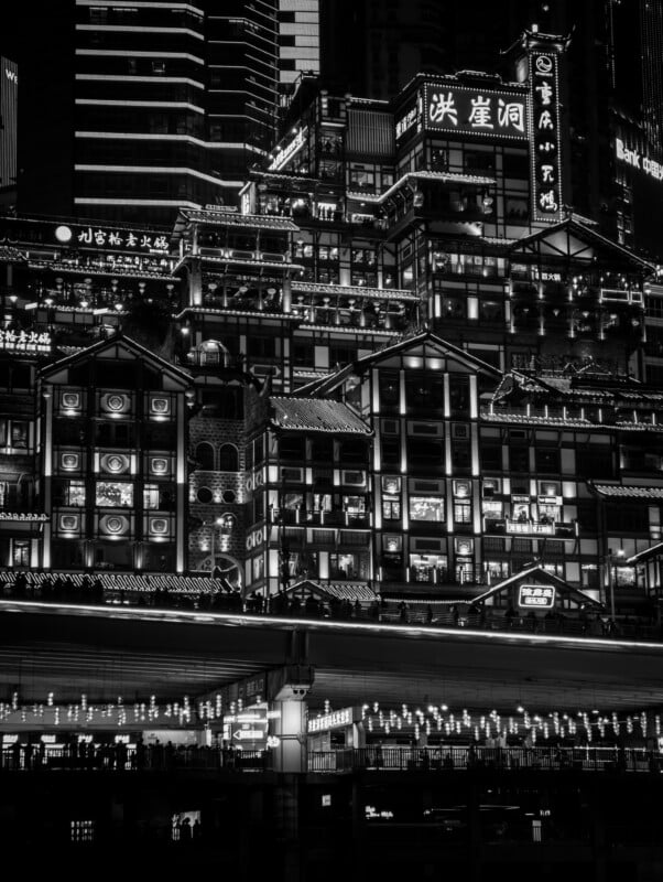 Black and white photo of a multi-story building at night featuring neon signs with Chinese characters and decorative lights, set against a backdrop of modern skyscrapers.