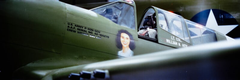 Close-up of a vintage military aircraft with olive-green paint, featuring a painted portrait of a woman on the side and a person in the cockpit. The U.S. Army markings and a white star insignia are visible.