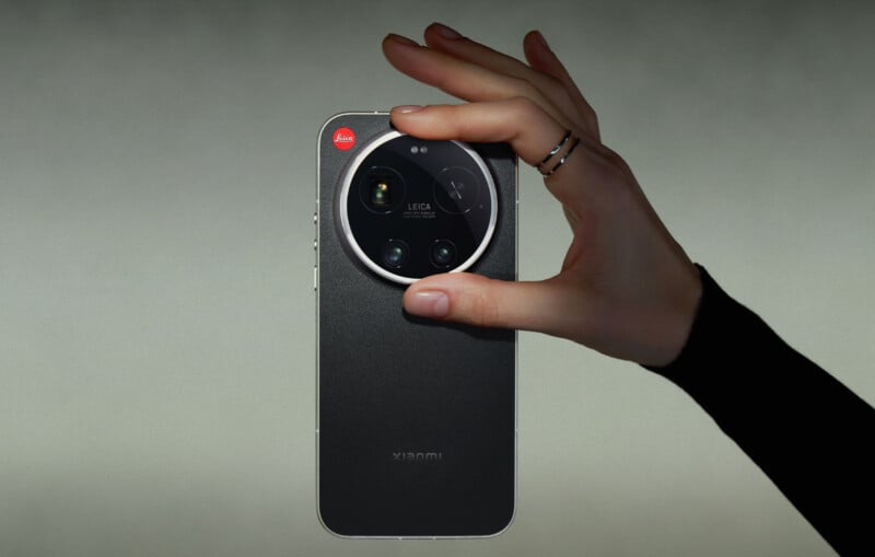 A hand with rings holds a black Xiaomi smartphone with a large, round Leica camera module on the back against a gradient background.