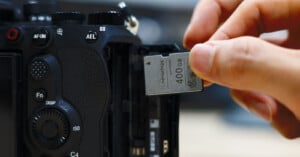 A hand inserts a 400GB memory card into the open memory card slot of a black digital camera.