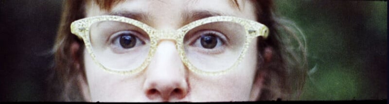 Primer plano del rostro de una persona, centrándose en sus ojos, con gafas grandes, translúcidas y estampadas. El fondo es de un verde borroso, lo que llama la atención sobre las gafas y los ojos.