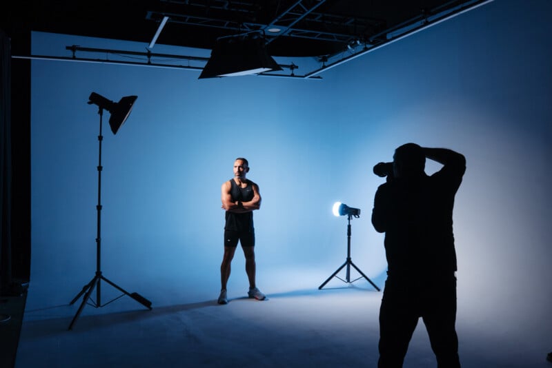 Un fotógrafo capturó una fotografía de un hombre en ropa deportiva posando en un estudio con luces azules, luces profesionales y equipo de fondo.