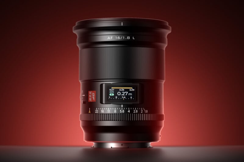 A close-up of a camera lens with a digital display showing focal distance, surrounded by a warm red gradient background. The lens markings read "AF 16/1.8 L," and various focus and aperture numbers are visible.