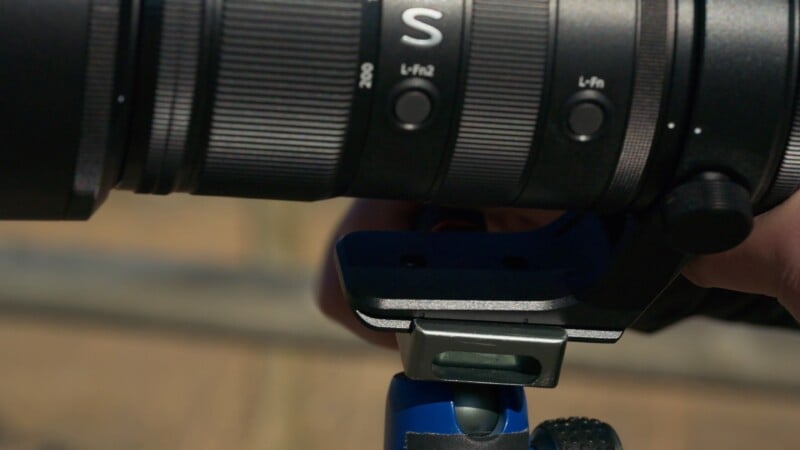 Close-up of a camera lens with labeled control buttons and textured grip, mounted on a tripod with a blue base.