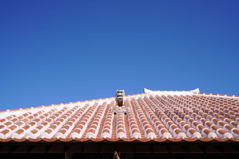 A traditional red-tiled roof with a decorative shisa statue at the peak, set against a clear blue sky.