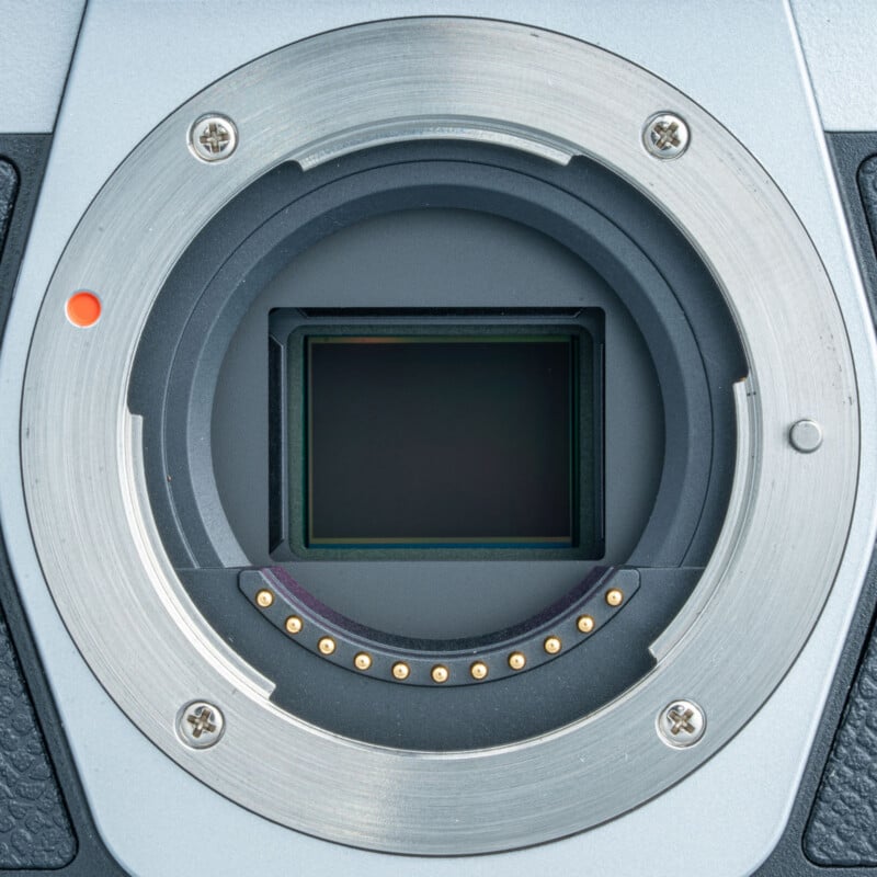 Close-up of a digital camera body showing the exposed image sensor and metal lens mount with electronic contacts around the edge.