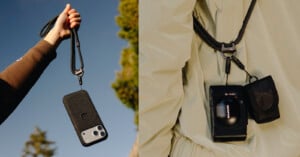 A hand holds a smartphone on a black lanyard against the sky, while another lanyard secures a camera and small pouch to a person in a light-colored jacket.
