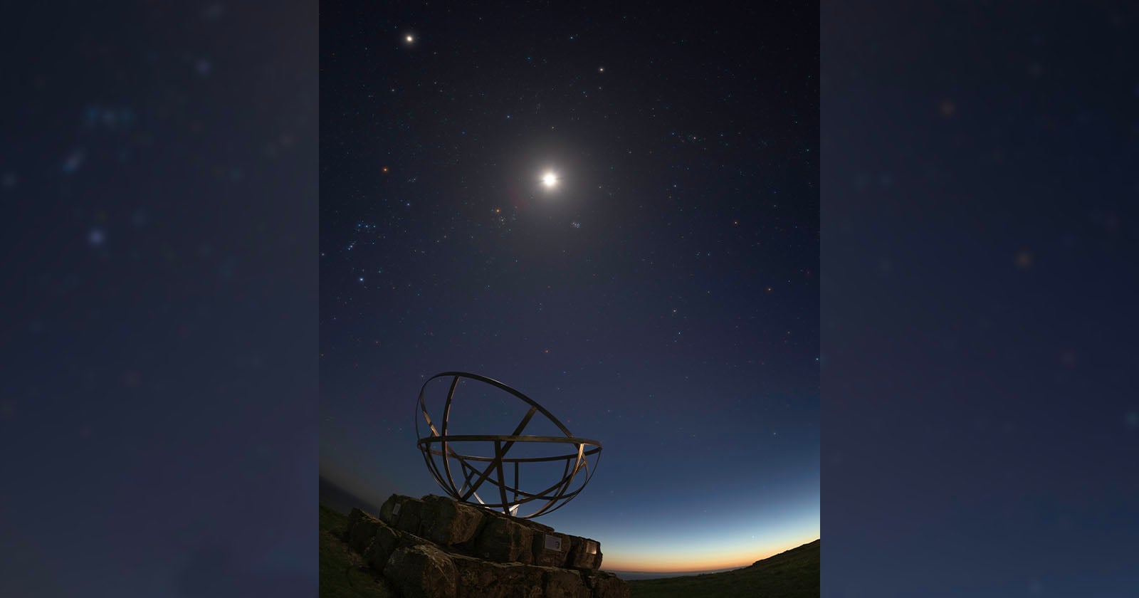 A metal sculpture shaped like a sphere stands on stone blocks under a night sky filled with stars, with a bright moon glowing near the center and a faint glow on the horizon.