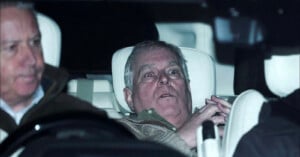 Two older men sit in the front and back seats of a car at night. The man in the back seat appears surprised or alarmed, looking ahead with wide eyes and hands clasped. The image is taken from outside the car.
