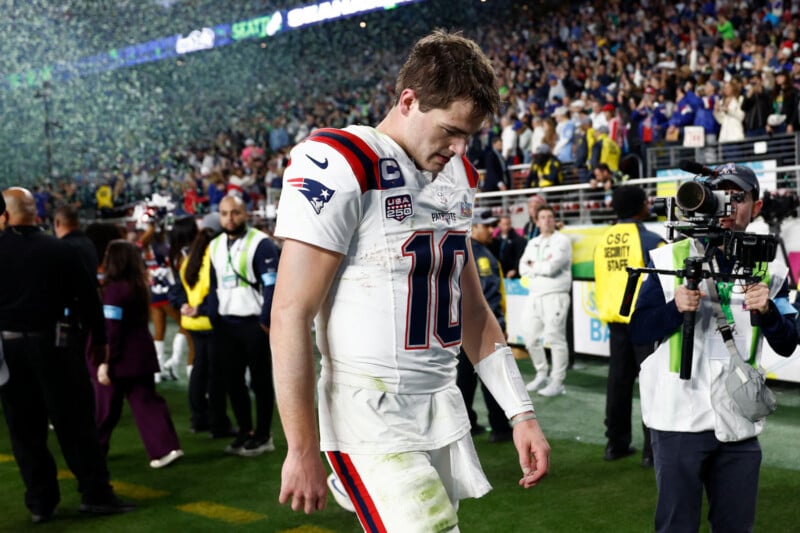 Un jugador de fútbol con camiseta blanca y el número 10 camina por el campo con la cabeza gacha, rodeado de cámaras y una multitud, con confeti cayendo y la multitud mirando de fondo.