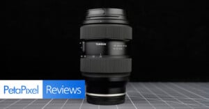 A Tamron 35-150mm F/2-2.8 camera lens stands upright on a grid-patterned surface with a black background. “PetaPixel Reviews” appears in blue and white at the bottom left corner.