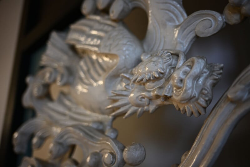 Primer plano de una escultura de dragón plateada, brillante y adornada con escamas, garras y rasgos faciales detallados, montada sobre un fondo decorativo.