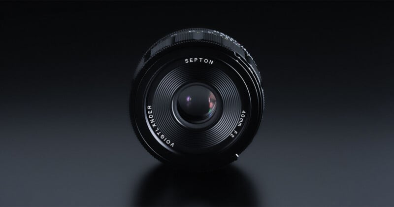 Foto de primer plano de la lente de la cámara Voigtländer Septon 40 mm f/2, colocada en posición vertical sobre una superficie reflectante oscura, con el cristal de la lente y los detalles claramente visibles.