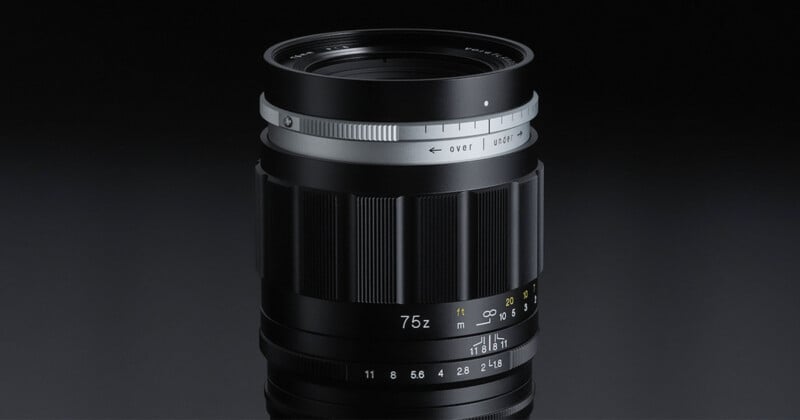 A close-up view of a black camera lens with a silver focus ring, detailed focus and aperture markings, set against a dark background.