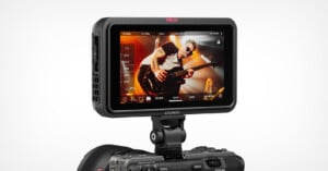 A camera monitor displays a video of a guitarist performing energetically on stage. The monitor is mounted on top of a camera, and various control icons and settings are visible on the screen.