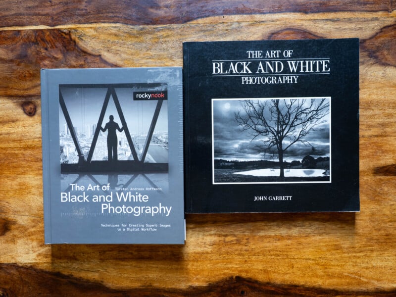 Two books on a wooden surface: "The Art of Black and White Photography" by Torsten Andreas Hoffmann (left) and "The Art of Black and White Photography" by John Garrett (right), each with a black and white cover image.