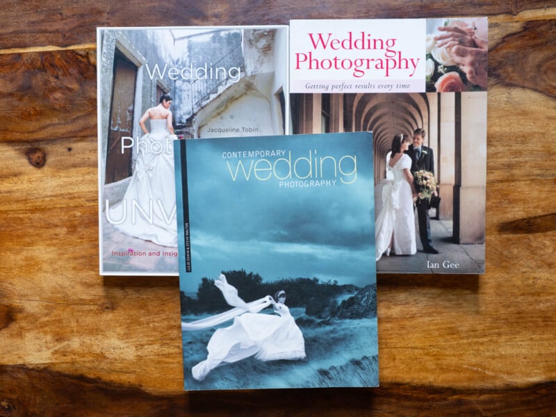 Three wedding photography books are arranged on a wooden surface, each featuring a bride and groom on the cover in different settings and styles.