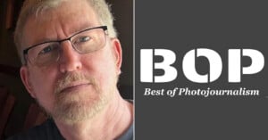 A man with light hair, glasses, and a beard looks at the camera; next to him is a gray background with the white text "BOP Best of Photojournalism.
